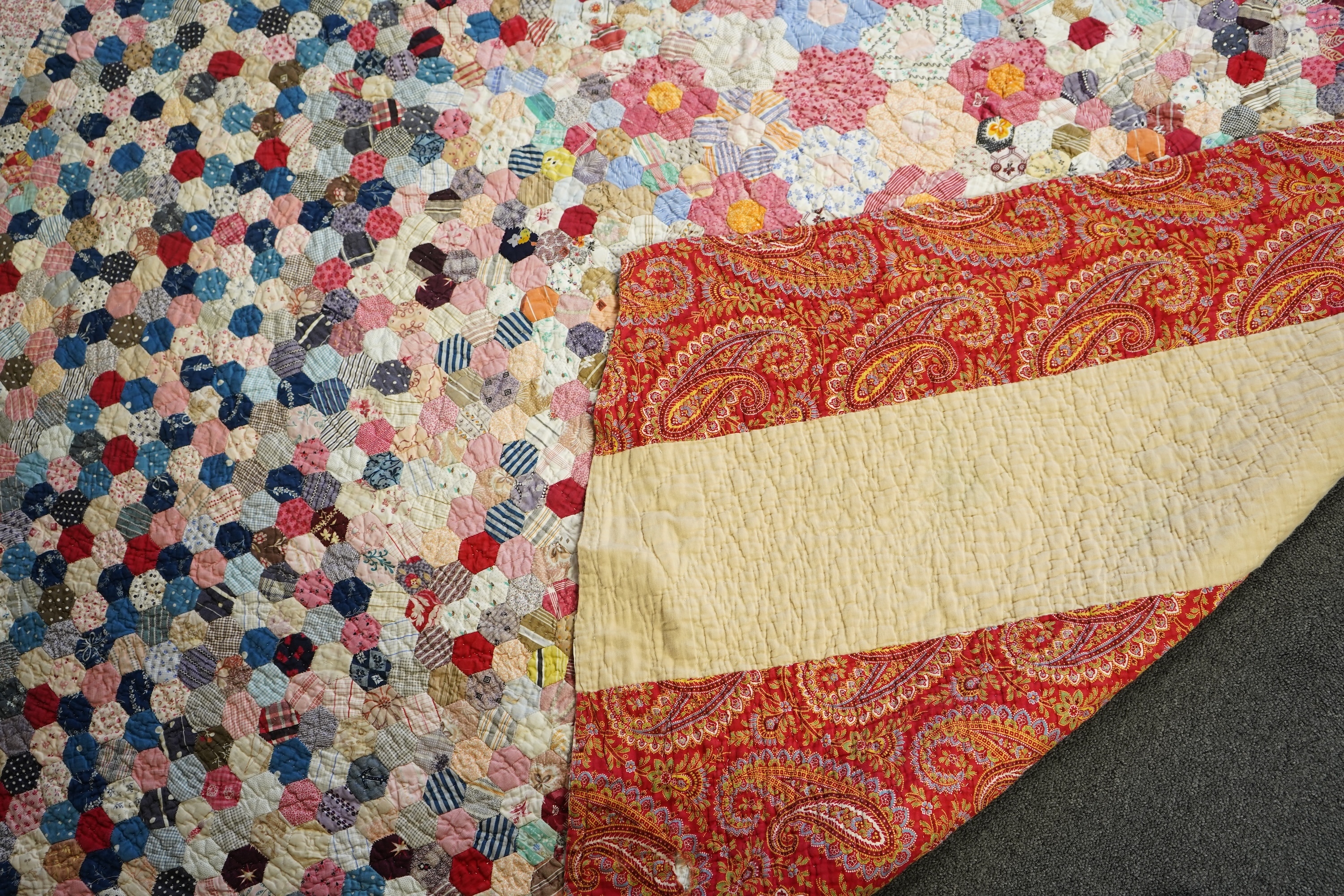 An English cotton hexagon hand made and hand pieced quilt, made from a large variety of printed dress fabrics from 19th century. The quilt edged with a wide stripped multi fabric border. The under side designed in wide s